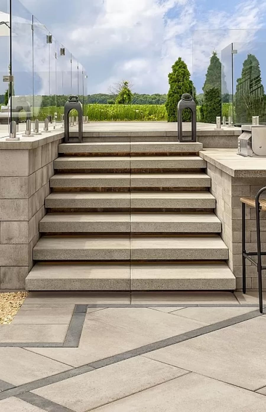 Patio starts with light beige pavers and flagstone leading to a patio with a glass railing.