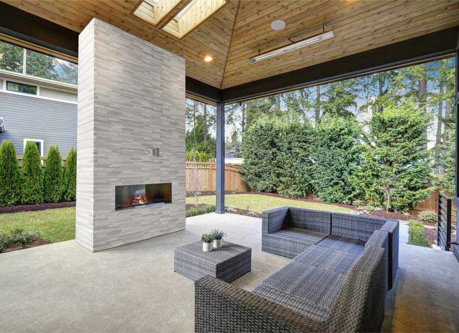 Covered outdoor patio area with wicker furniture and a brick wall with a fireplace built in